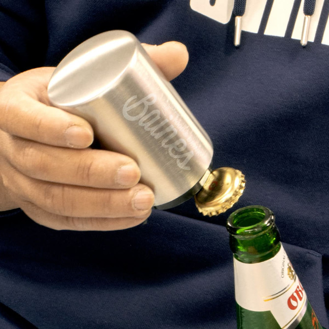 A drink bottle opener in silver, featuring a rounded design and a branding logo, being used to open a green bottle.
