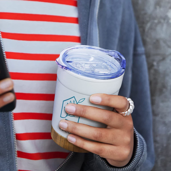 A double wall cup in a white and wood finish, featuring a transparent lid and held by a person in a striped shirt.