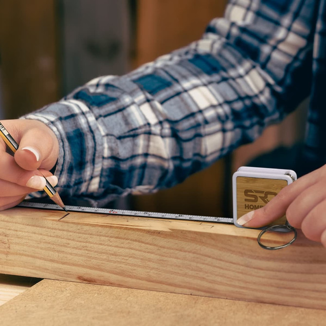 A bamboo tape measure key ring in use, featuring a measuring tape and a wooden ruler on a work surface.