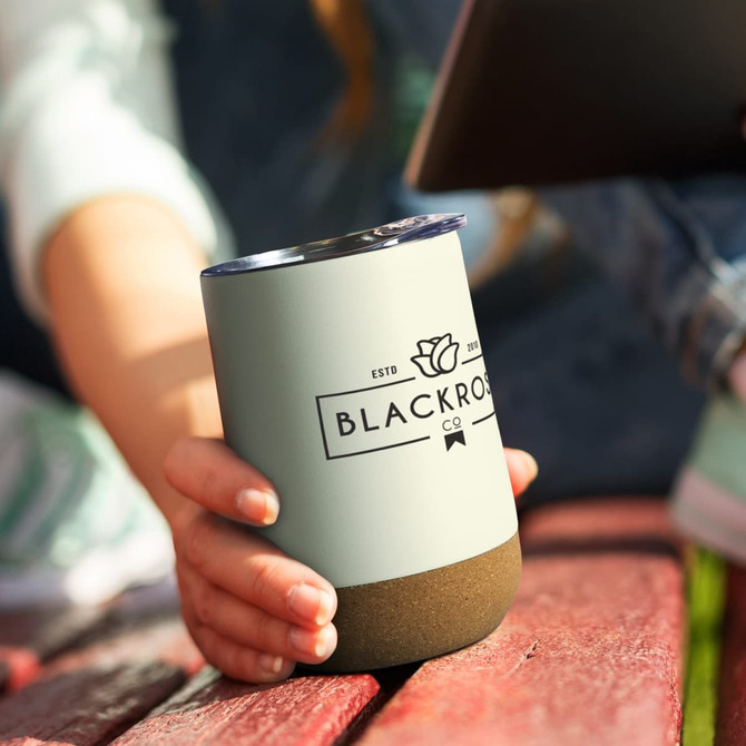 A drink bottle in matte green with a textured base, featuring a logo. Held by a person on a wooden surface.