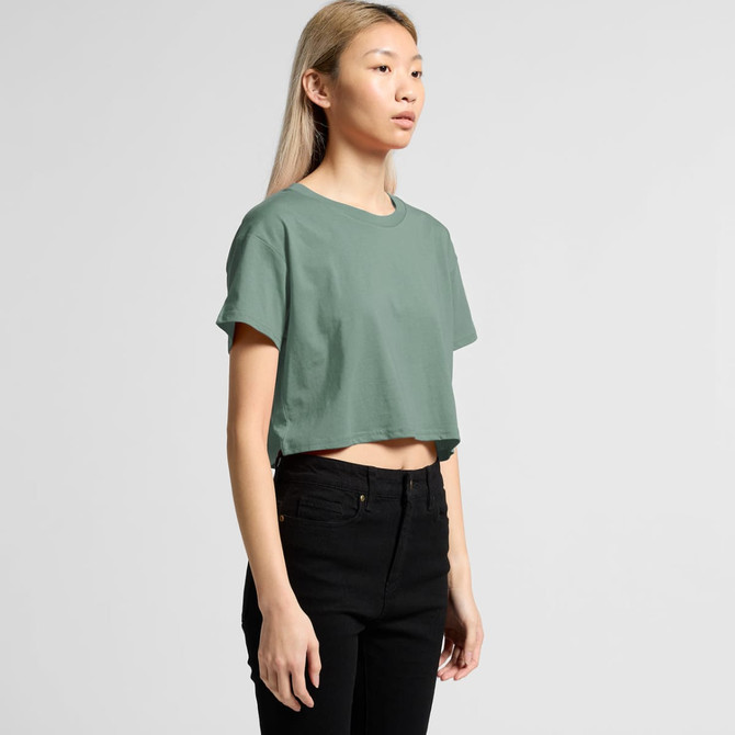 A cropped green t-shirt with short sleeves, displayed on a model wearing black jeans, featuring a subtle logo.