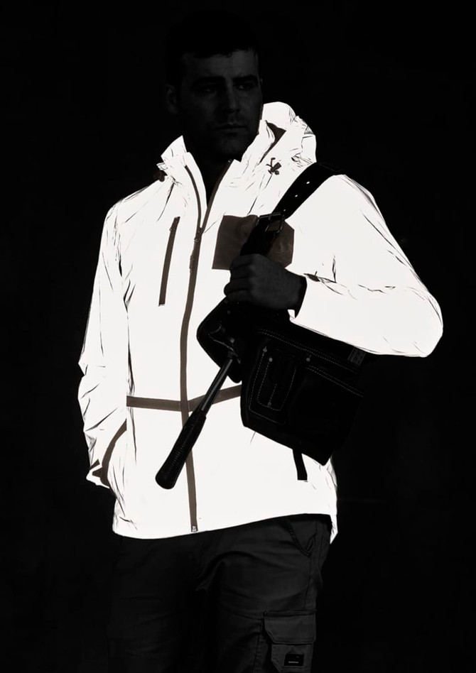 A reflective waterproof jacket in white, featuring a hood and pockets, worn by a model holding a bag.