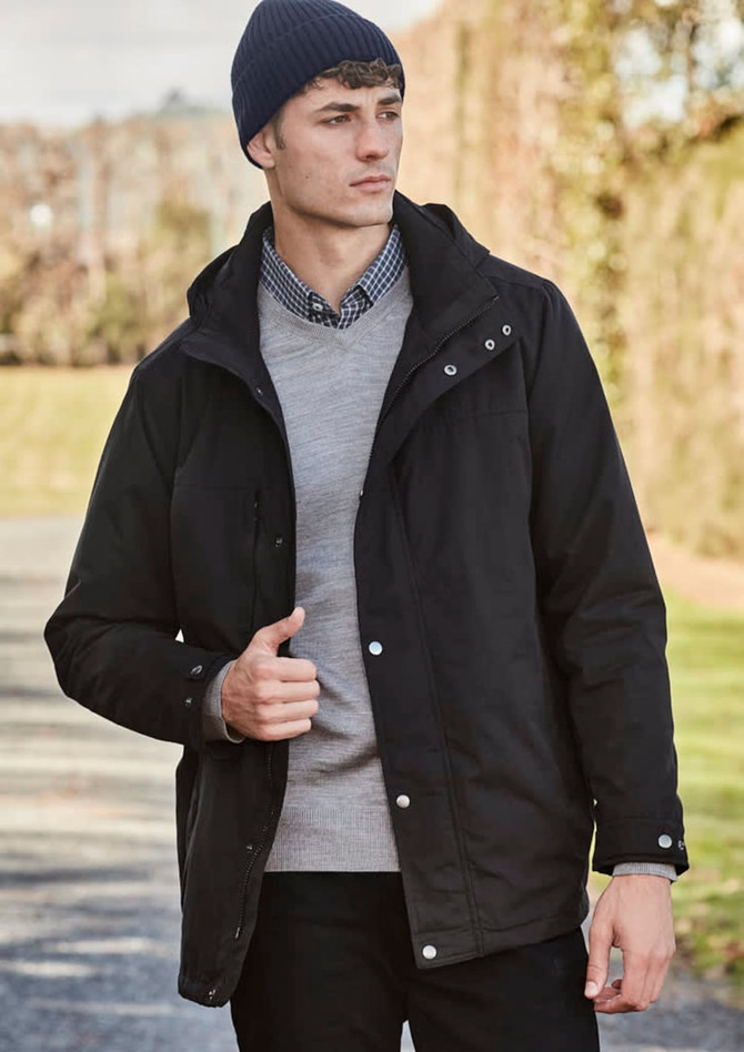 A model wearing a black jacket and a navy beanie, standing outdoors with greenery in the background.