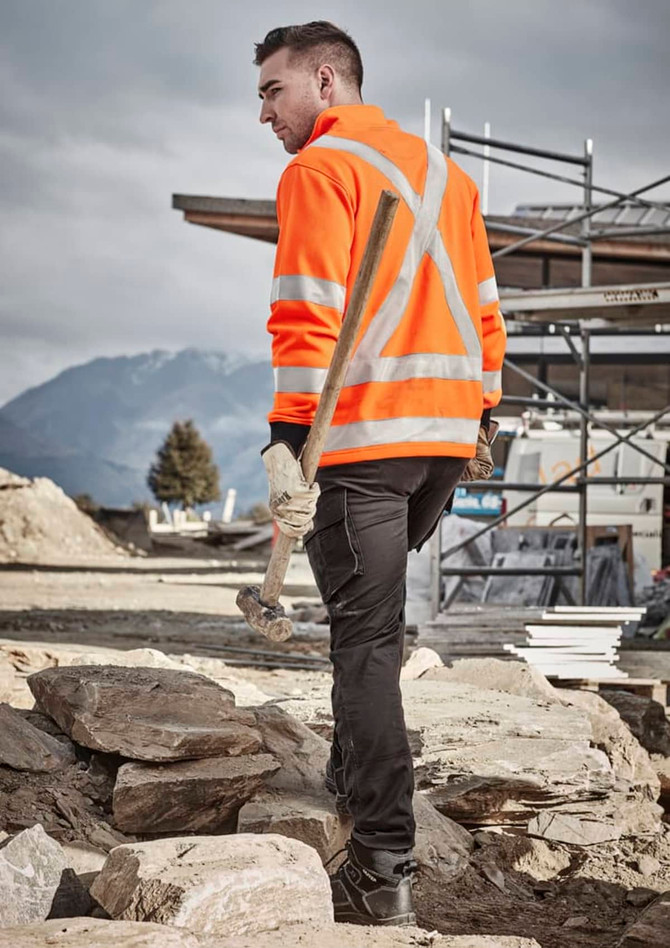 A unisex hi vis orange jumper with reflective X-back stripes, set against a construction site backdrop.