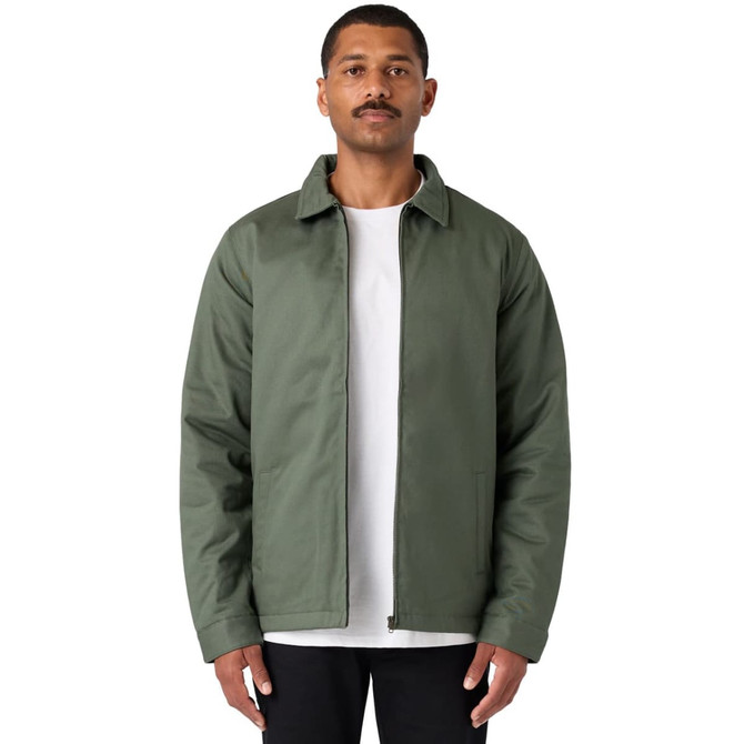A man wearing a green service jacket over a white t-shirt, standing with a neutral expression. The jacket has a logo.