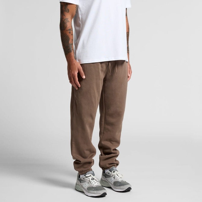 A pair of brown track pants with a relaxed fit, paired with light grey sneakers. The model is wearing a plain white t-shirt.
