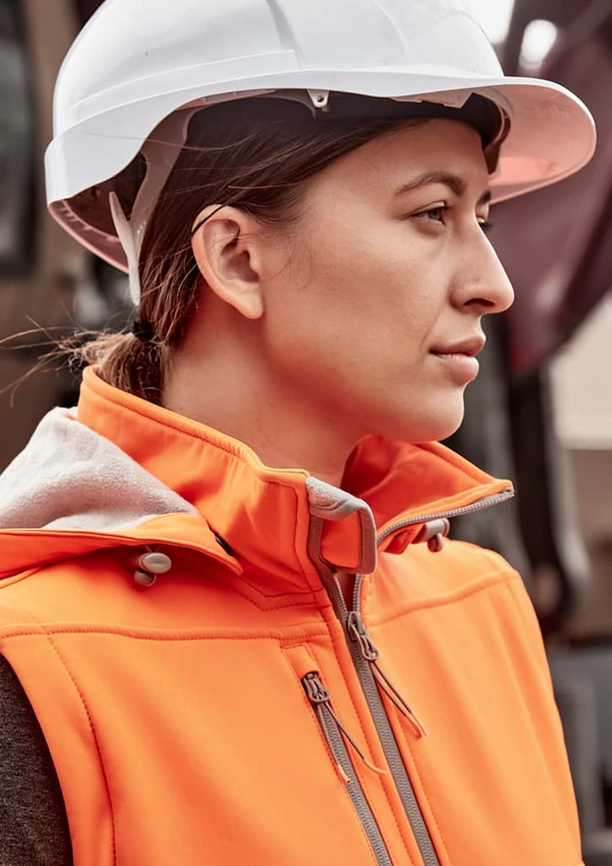 An orange women's softshell jacket with a zipper, worn by a woman in a white hard hat.