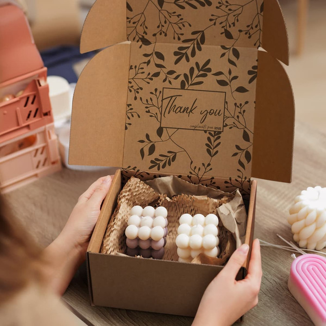 A brown die cut box with a locking lid, featuring a decorative interior and filled with shaped candles.