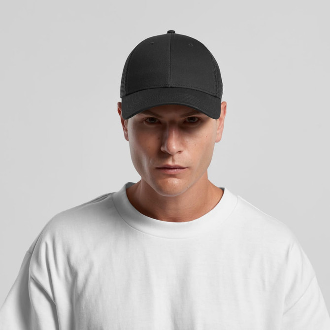 A black trucker cap with a structured front panel and mesh back, worn by a model in a white t-shirt.