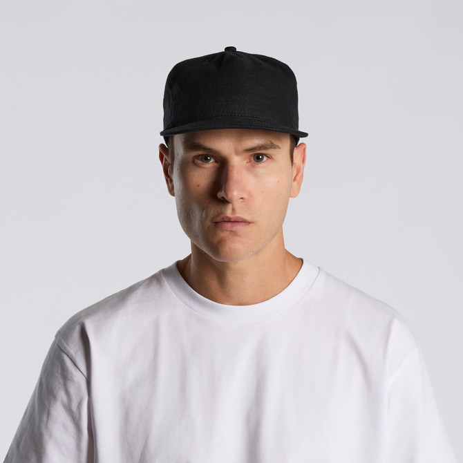 A black cap worn by a person in a white t-shirt, featuring a logo on the front.