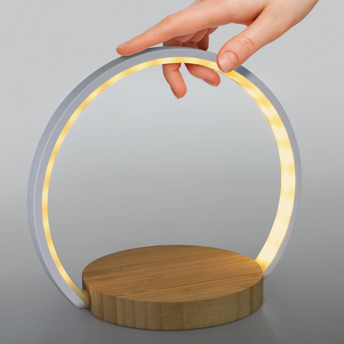 A wireless charging night light in a circular design with a white frame and a bamboo base, featuring warm glowing lights.