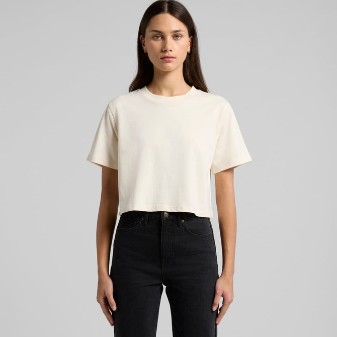 A cropped cream T-shirt with short sleeves, displayed on a model wearing black jeans. The shirt has a logo.