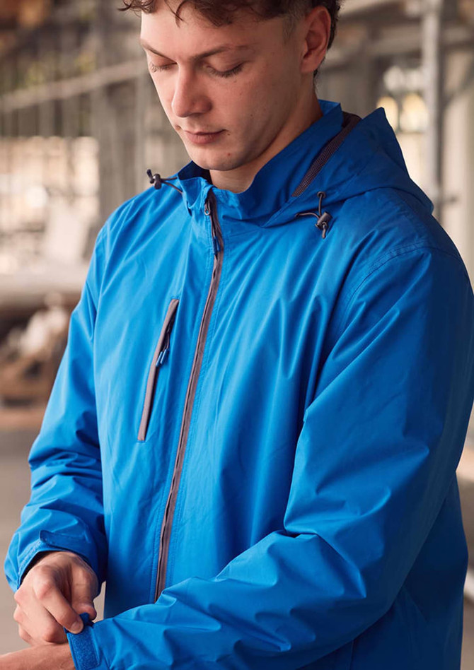 A man in a bright blue unisex rain jacket with a hood, standing indoors near construction. The jacket features a logo.
