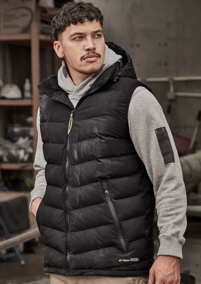 A black unisex hooded puffer vest worn over a grey sweatshirt, featuring a small logo and zip pockets.