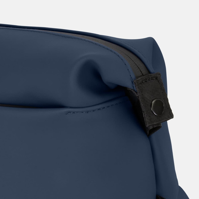 A toiletry bag in navy blue with a black zipper and a snap button detail. It features a sleek, soft-touch material.