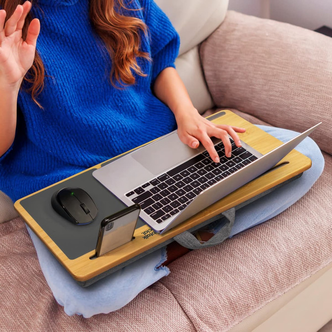 A bamboo lap desk with a grey surface, supporting a laptop and mouse, held by a seated person in a blue sweater.