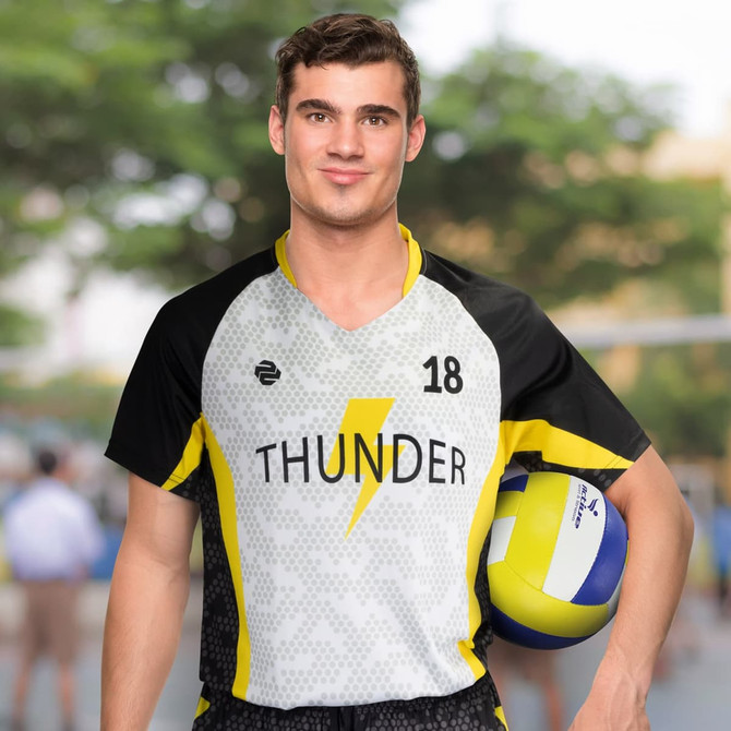 A man in a black and yellow volleyball jersey, holding a volleyball, with a blurred outdoor background.