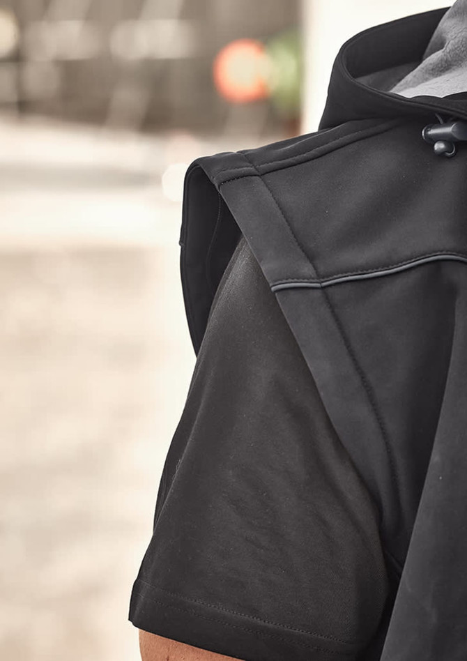A close-up of a black unisex softshell jacket, highlighting the shoulder and sleeve design. It features a logo.