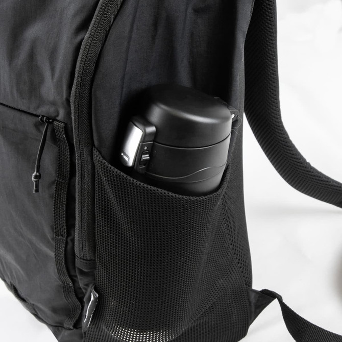 A black daypack features a side mesh pocket holding a black drink bottle. The bag has zippers and adjustable straps.