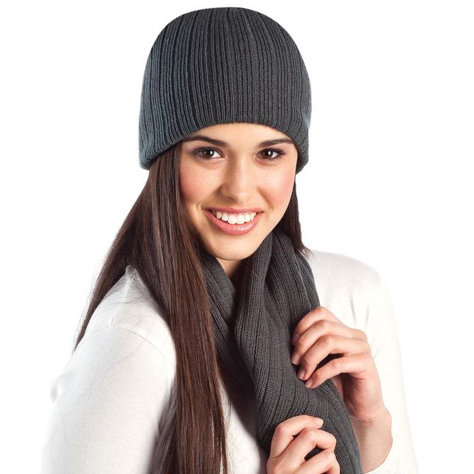 A cable knit beanie in grey worn with a matching scarf, displayed on a smiling model.