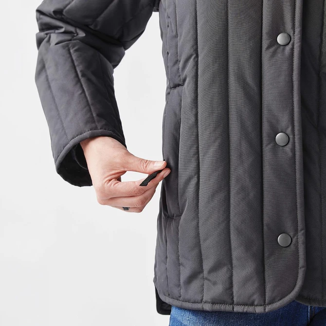 A thermal jacket in grey featuring a quilted design and a hand reaching into a side pocket. It has a logo.