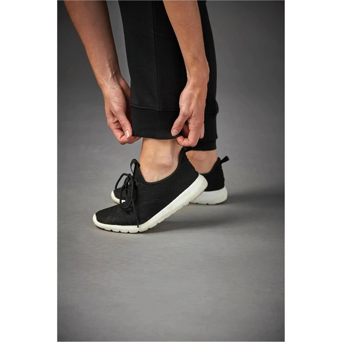 A person adjusts the hem of black Yukon track pants while wearing black trainers with a white sole.