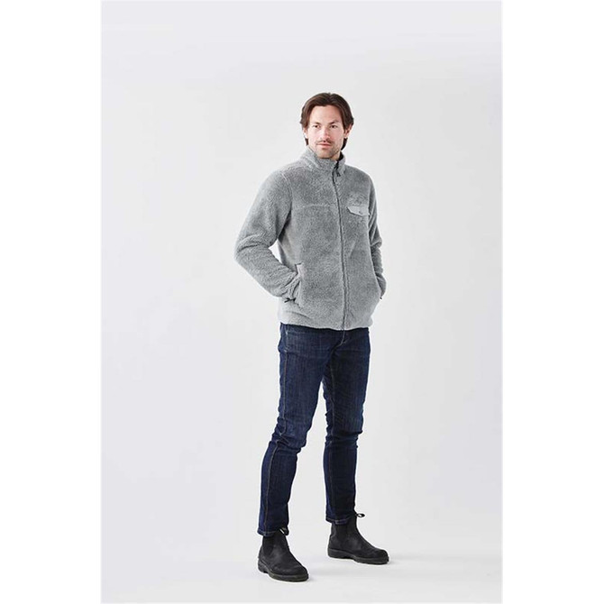 A men's grey Bergen Sherpa fleece jacket is displayed on a model, featuring a logo on the chest. The model wears dark jeans and boots.