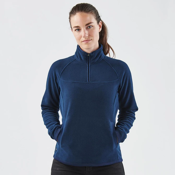 A navy blue women's fleece jumper with a 1/4 zip and a logo on the side. The model is posing with hands in pockets.