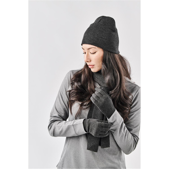 A knit beanie in black, styled with matching gloves and a long scarf, set against a neutral background.
