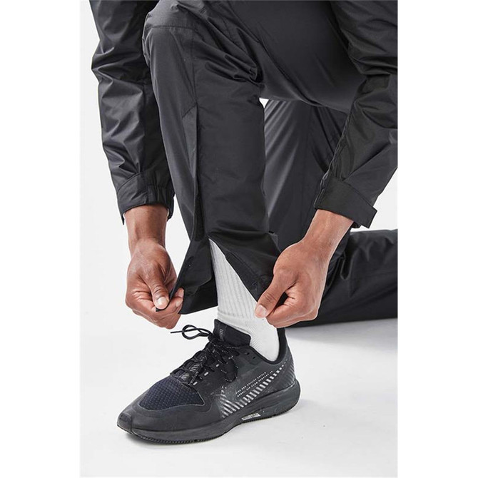 Men's Olympia Rain Pant in black, featuring adjustable leg cuffs, being worn with a black sneaker and white socks.