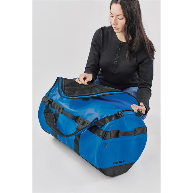 A blue duffle bag with black accents and a logo, being opened by a person in a black top.