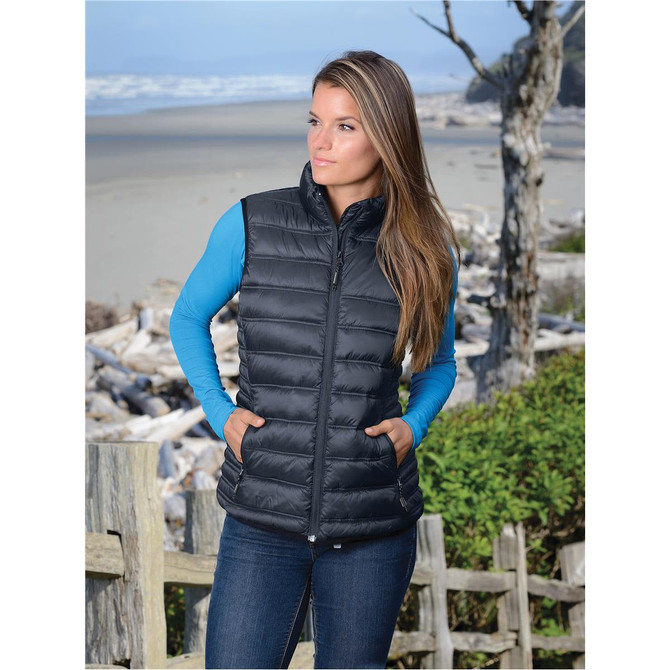 A women's thermal vest in black, featuring a zip front and a fitted design, set against a coastal background.