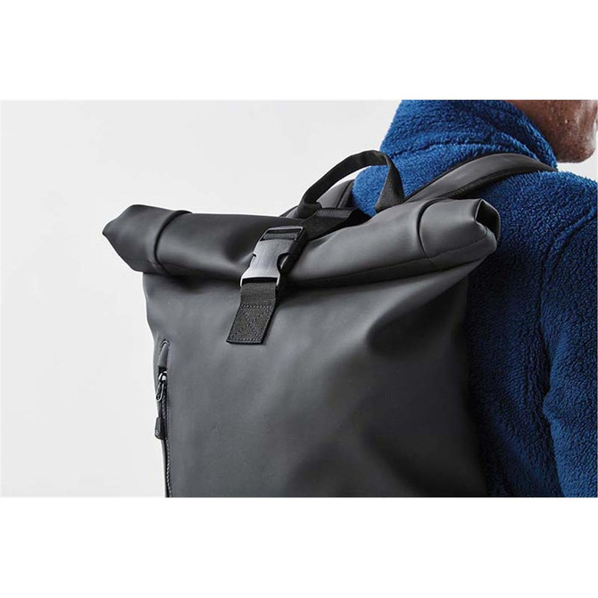 A black roll-top backpack with adjustable straps and a buckle fastening, worn on a person's back.