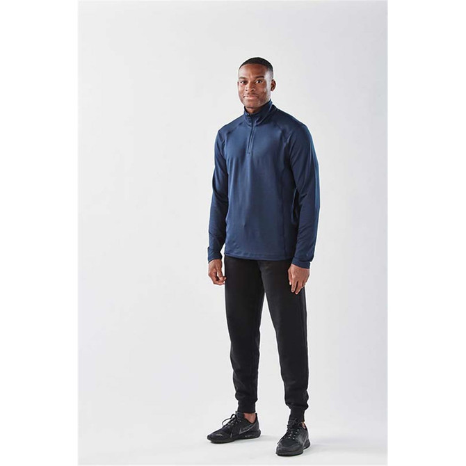 A model in a navy long sleeve 1/4 zip shirt, paired with black pants and black shoes, standing against a plain background.