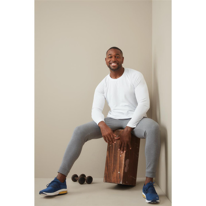 A man wearing a white long sleeve shirt sits on a wooden block, paired with grey pants and blue sneakers, with weights nearby.