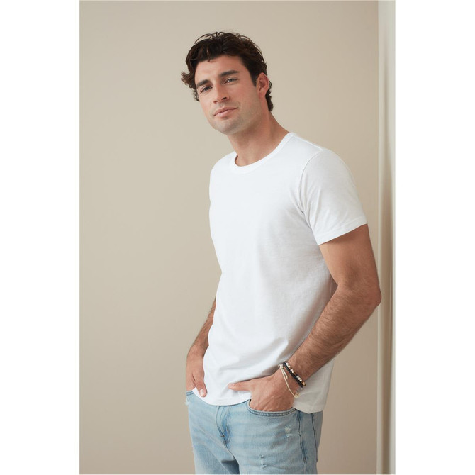 A white crew neck t-shirt worn by a man, paired with light blue jeans. The shirt features a logo on the chest.