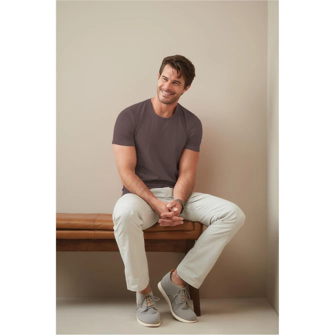 A model sits on a bench, wearing a mauve crew neck t-shirt and light-coloured trousers with grey sneakers.