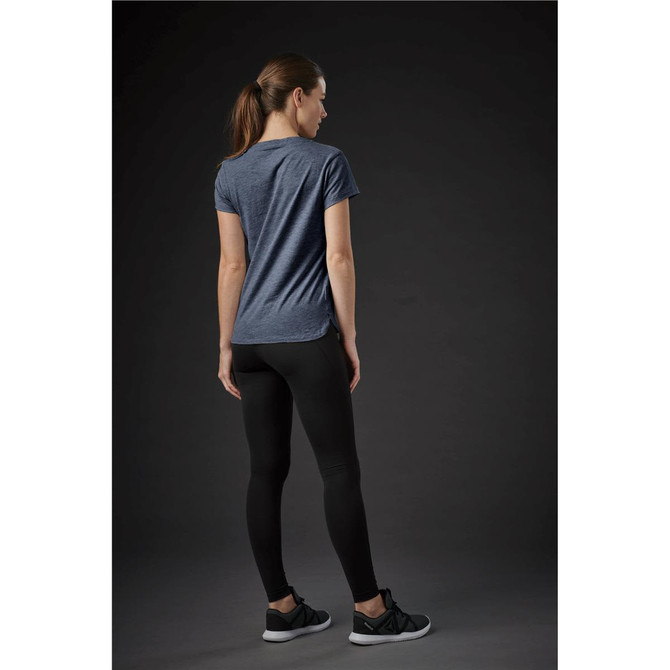 A woman wearing a navy blue crew neck tee paired with black leggings, standing against a dark background.