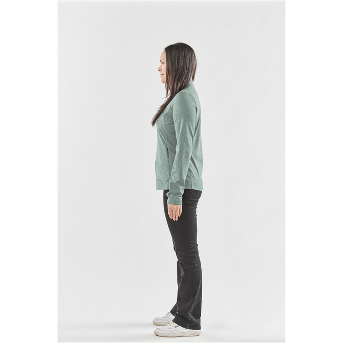 A side view of a woman wearing a teal performance jacket with long sleeves and black trousers.