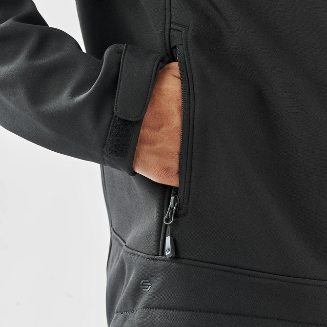A black softshell jacket with a zippered pocket, featuring a hand reaching inside the pocket.