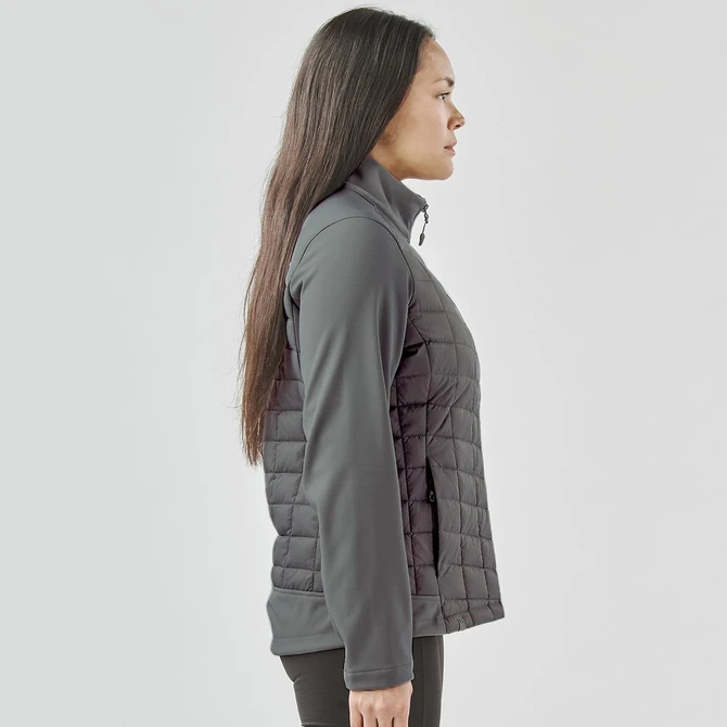 A women's softshell jacket in grey, featuring a quilted design and a zip closure. The jacket includes a logo.