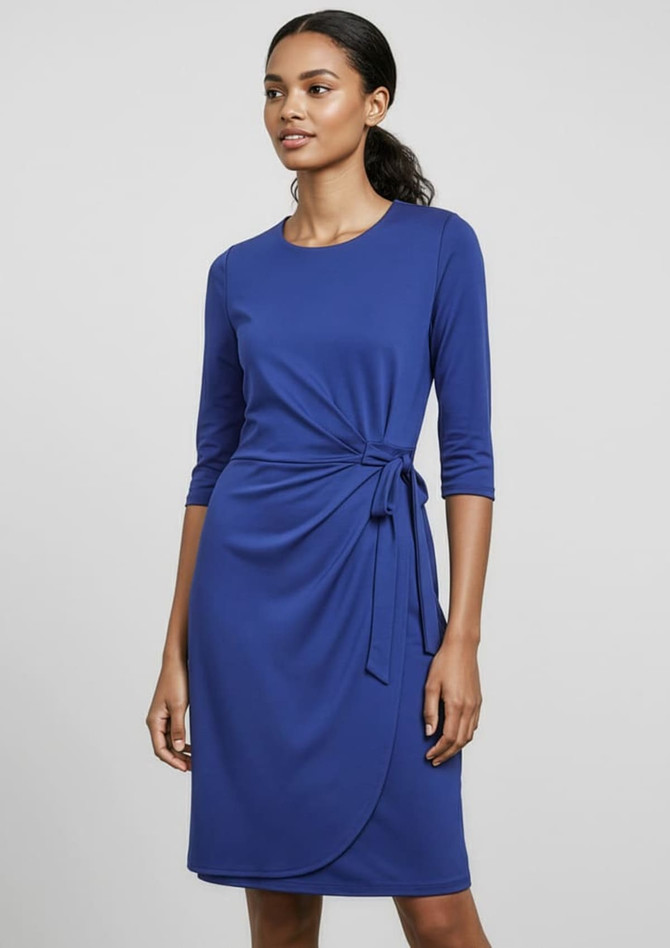 A blue women's dress features three-quarter sleeves and a tied waist detail, set against a neutral background. It has branding.
