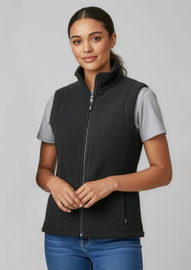 A women's plain micro fleece vest in black, featuring a front zipper and a high collar. Model wears a grey shirt underneath.