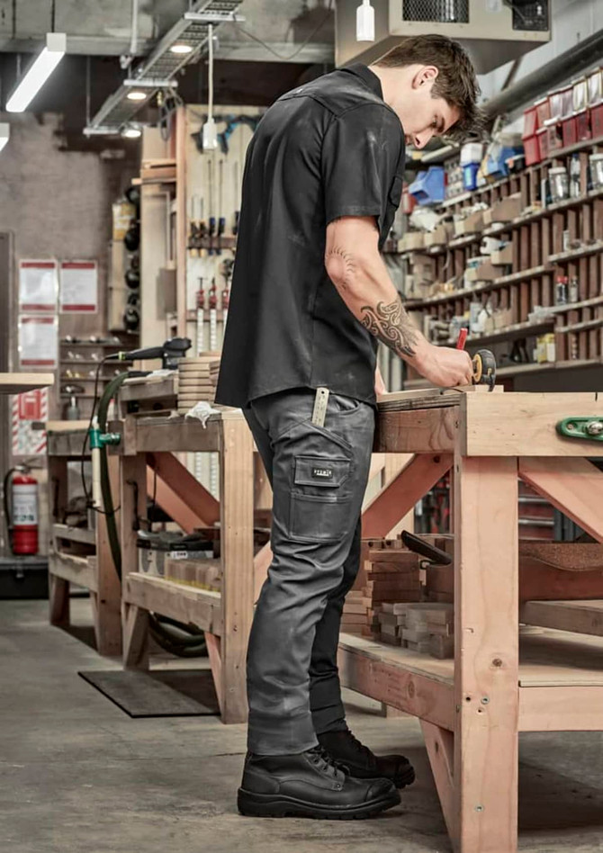 Men's essential basic stretch cargo pants in grey, featuring pockets and a logo, worn by a person in a workshop setting.