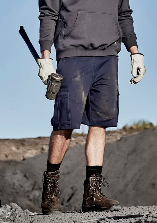 A pair of navy blue men's cargo shorts with multiple pockets, being worn by a person holding a tool.