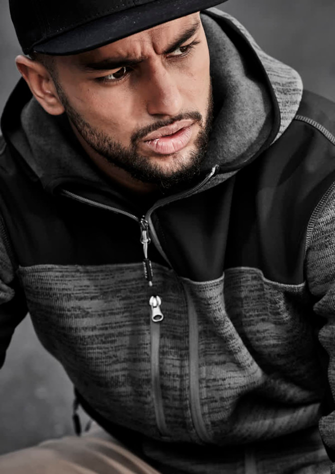 A man is wearing a black and grey unisex hoodie featuring a zip-up front and a hood. The garment has a logo.