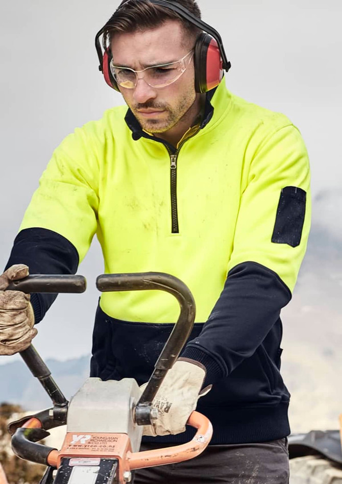A unisex hi-vis yellow and navy 1/2 zip pullover, featuring a logo and worn by a person operating machinery.