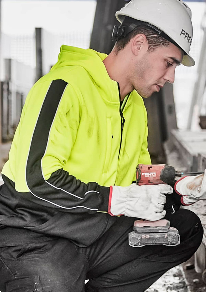 A unisex high visibility full zip hoodie in bright yellow with black accents, worn by a person holding a drill.