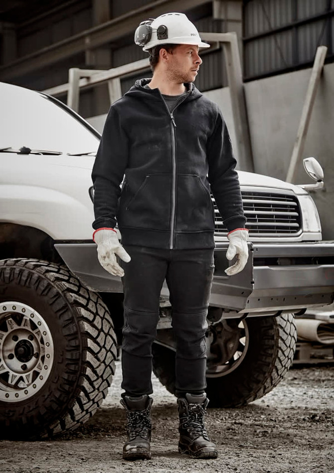 A man wearing a black unisex zip front multi-pocket hoodie, gloves, and work boots, standing next to a white vehicle.