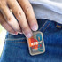 A compact case holding foam earplugs, featuring a logo design and a blue cord, displayed in a person's pocket.